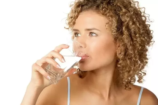 La jeune fille suit un régime pour les paresseux, buvant un verre d'eau avant de manger